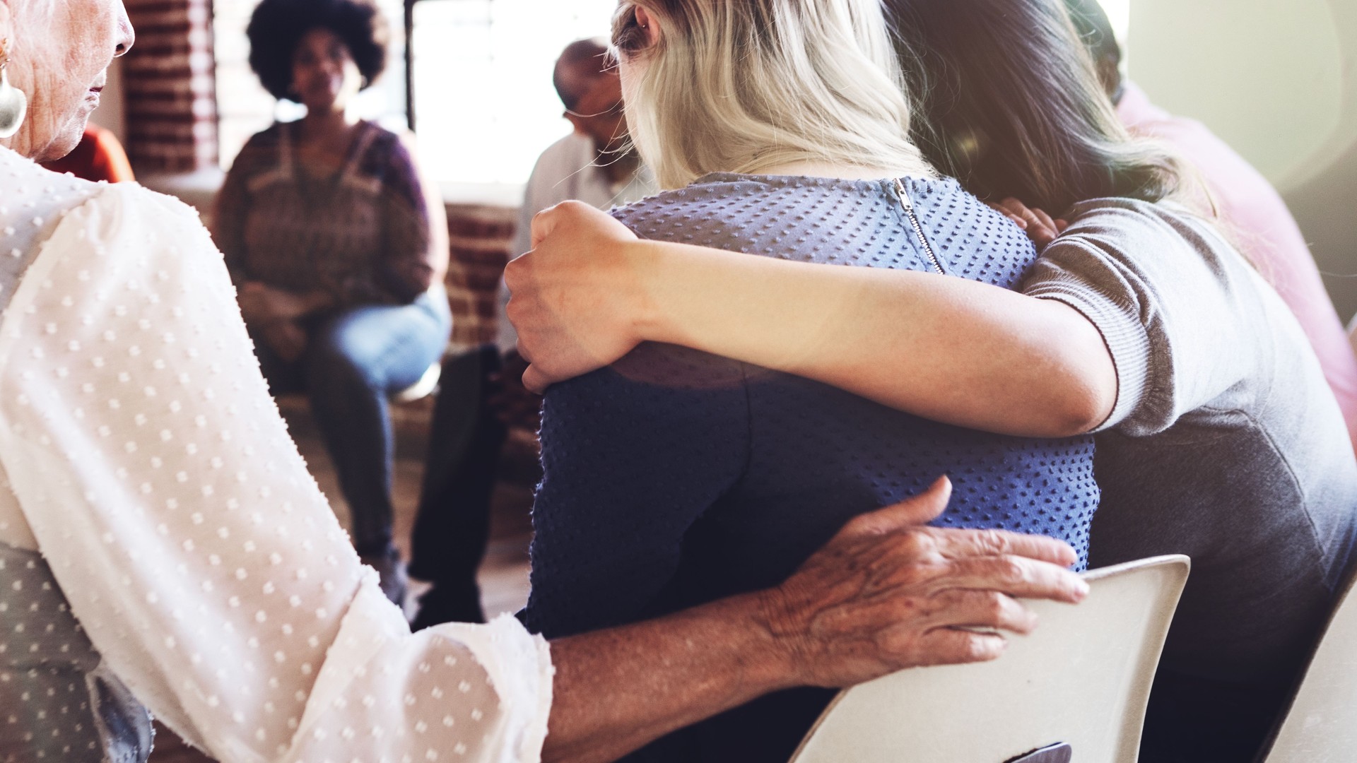 Support group meeting with diverse individuals sitting in a circle hugging and supporting one another.