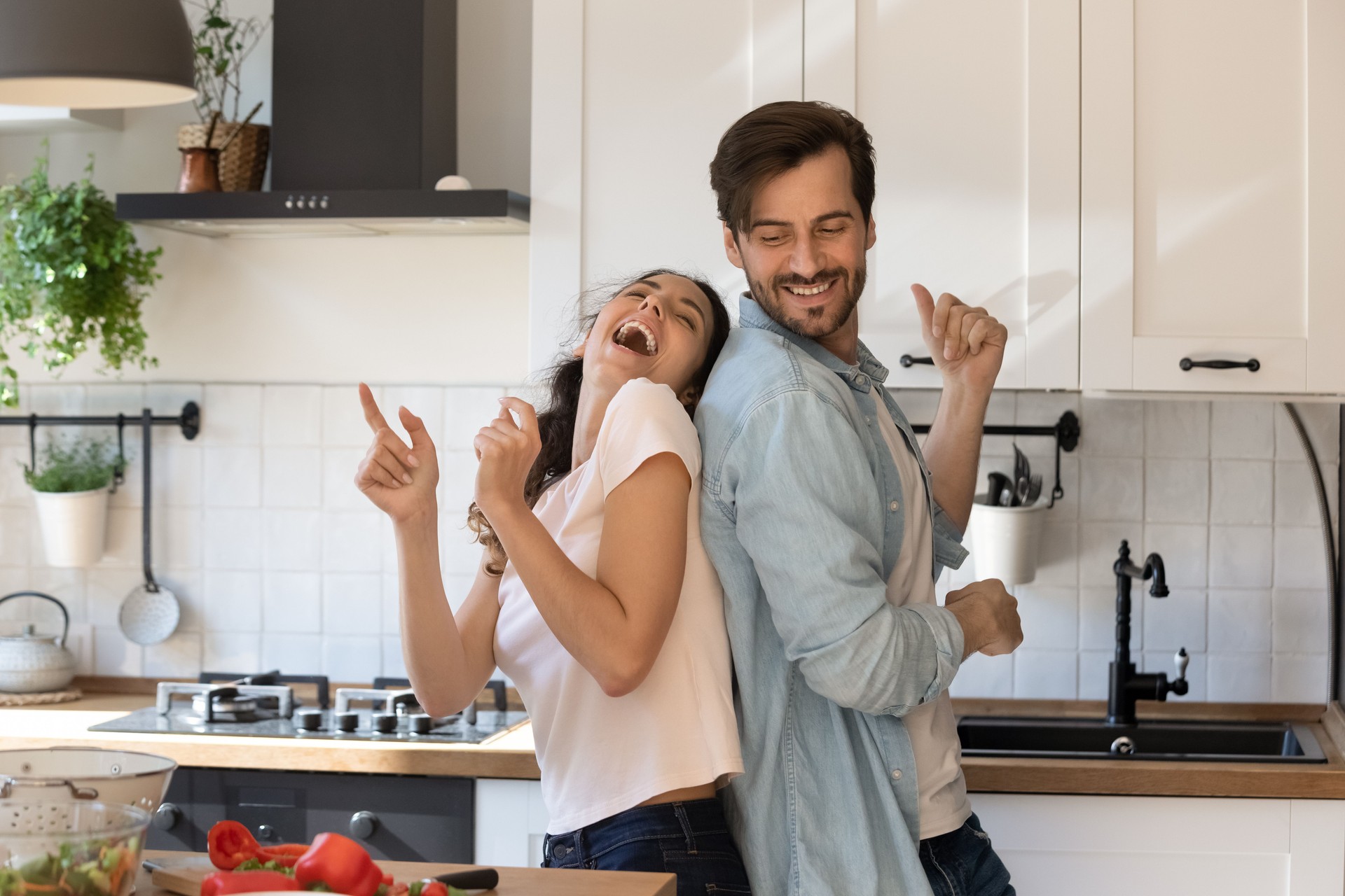 Overjoyed young family having fun in modern kitchen, dancing, laughing