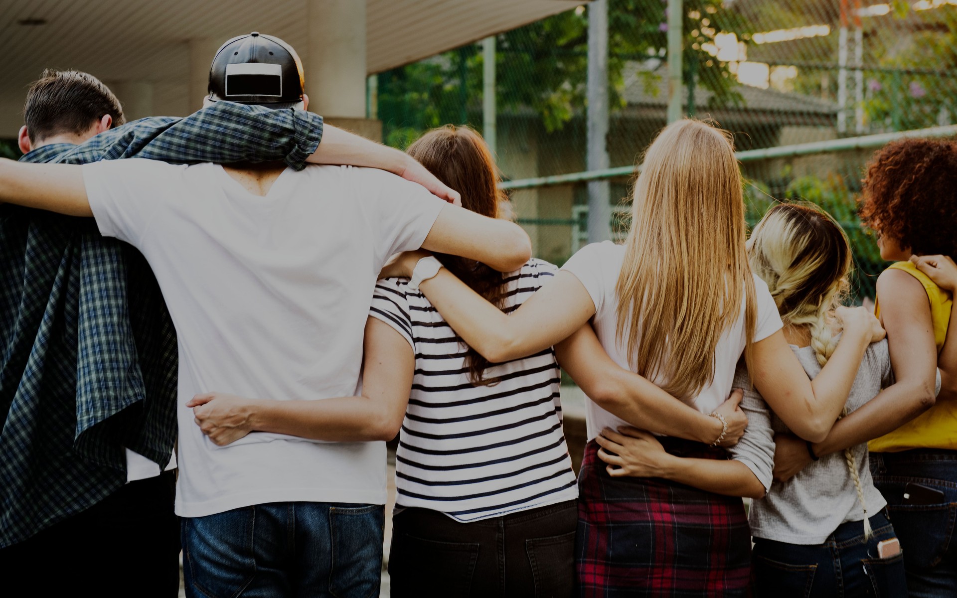 Smiling happy young adult friends arms around shoulder outdoors friendship and connection concept